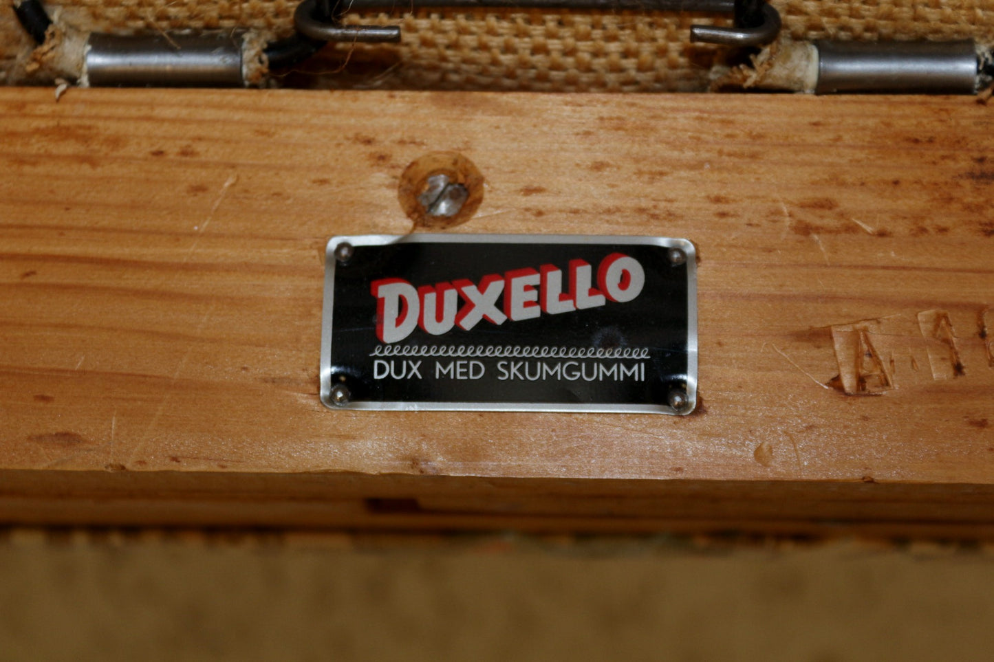 Black Duxello label with red text on a light wooden furniture frame.