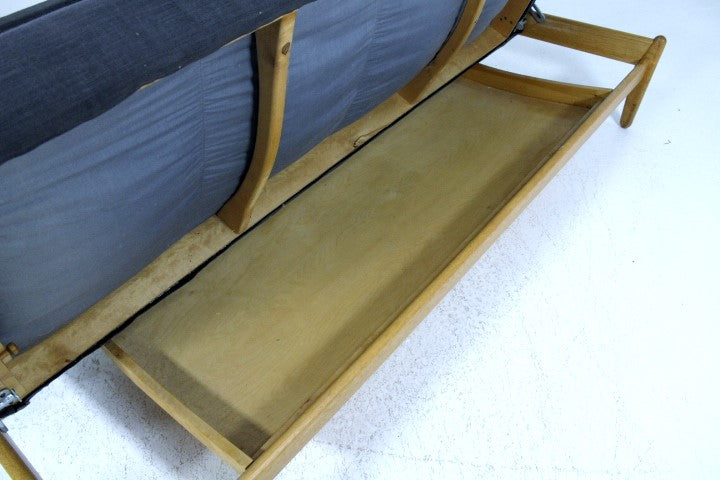 Underside view of a vintage wooden daybed with a dark blue upholstered top.