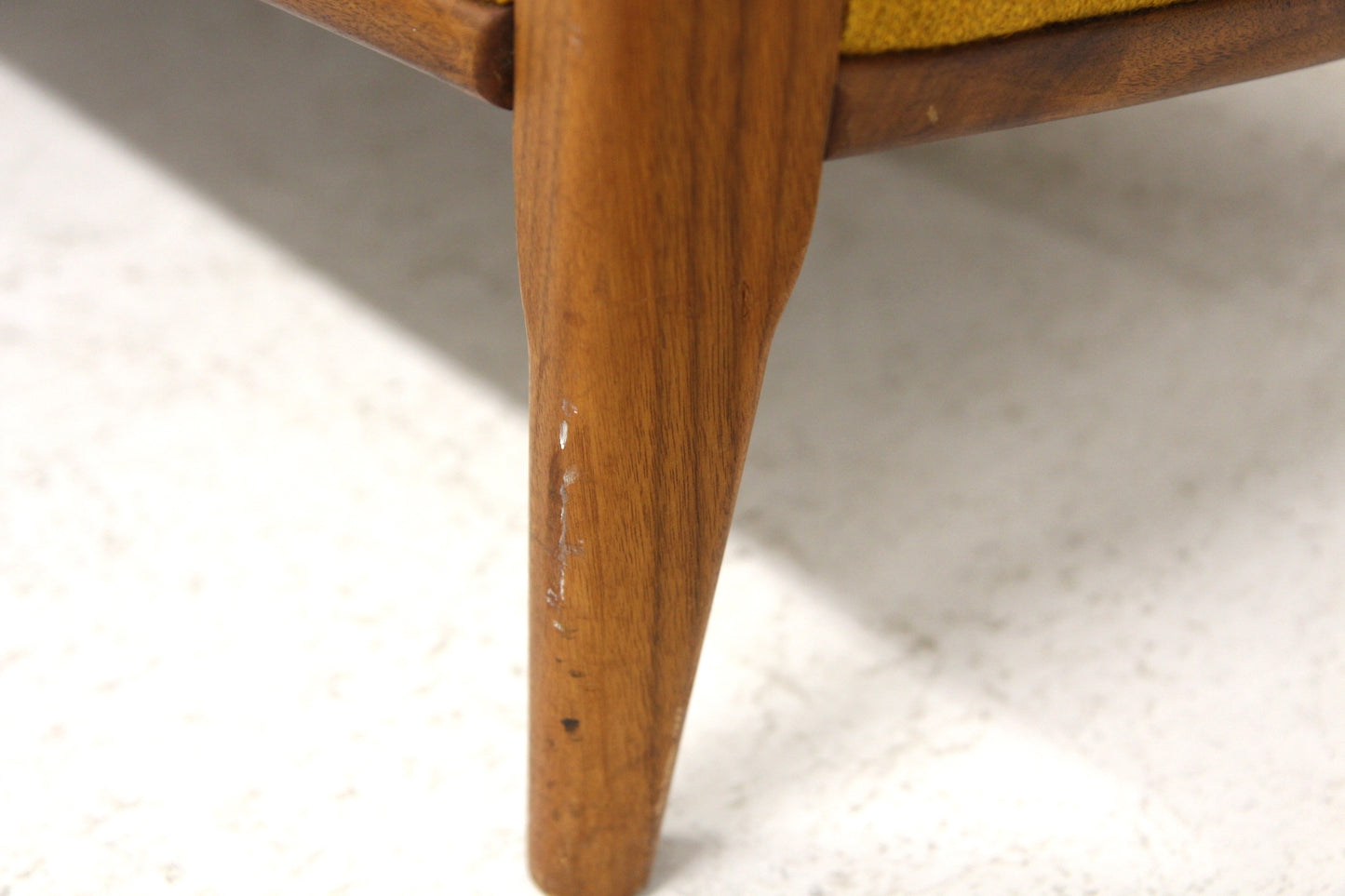 Tapered wooden leg of a vintage Scandinavian sofa with yellow upholstery.