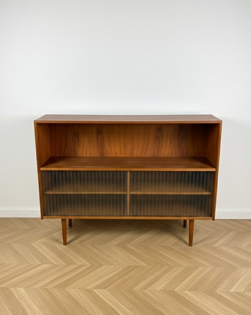 Libreria bassa danese anni 50 in teak, vista frontale, vano aperto superiore e ante scorrevoli in vetro plissettato, gambe affusolate coniche