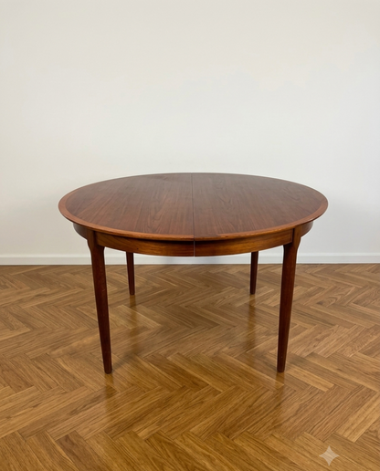 Tavolo da pranzo rotondo in teak design danese anni '60, Ø121 cm, quattro gambe affusolate, vista frontale pavimento parquet