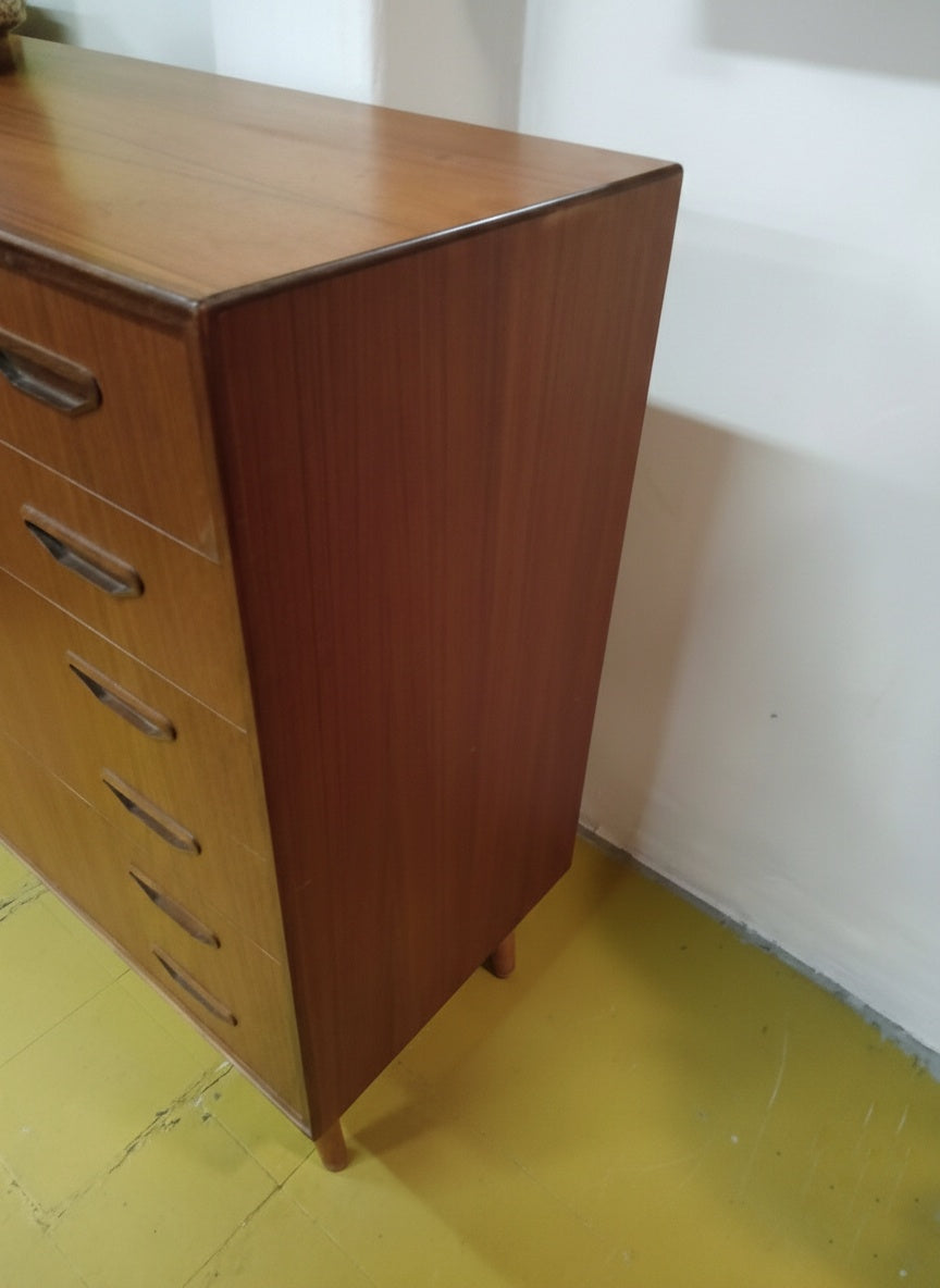 Vista laterale cassettiera teak danese anni 50, sei cassetti con maniglie intagliate e gambe affusolate, design scandinavo