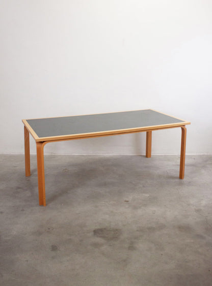 Vista 3/4 del tavolo vintage Magnus Olesen anni '50 — piano in linoleum grigio con cornice in legno chiaro, gambe in legno curvato