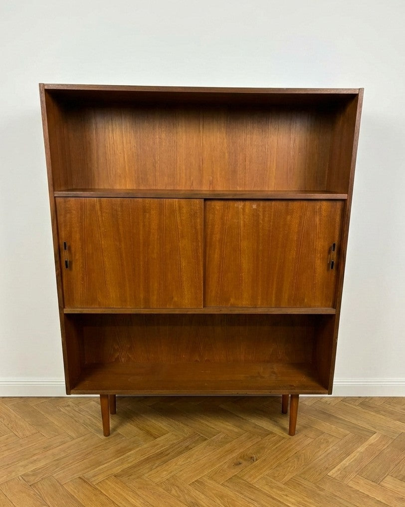Libreria danese anni 50 in teak, vista frontale, due ante scorrevoli con maniglie in metallo e ripiani aperti superiore e inferiore