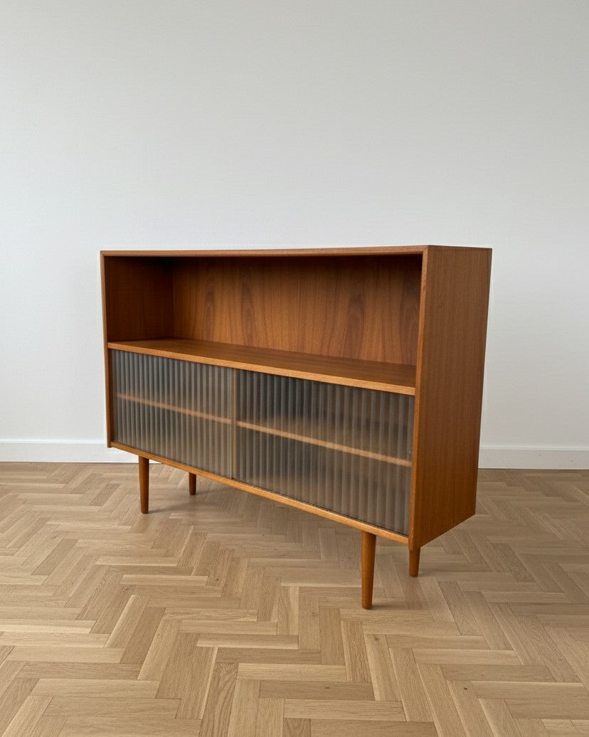 Libreria bassa danese teak anni 50, vista tre quarti, profilo della struttura e ante scorrevoli in vetro plissettato, gambe coniche