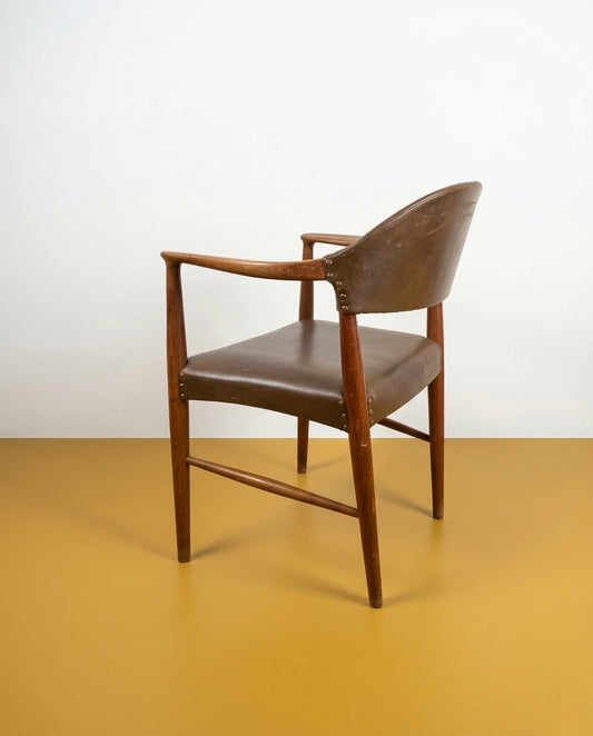 Poltroncina Kurt Olsen danese anni 60 in teak, vista posteriore tre quarti, schienale a guscio curvato e braccioli integrati, rivestimento in similpelle marrone