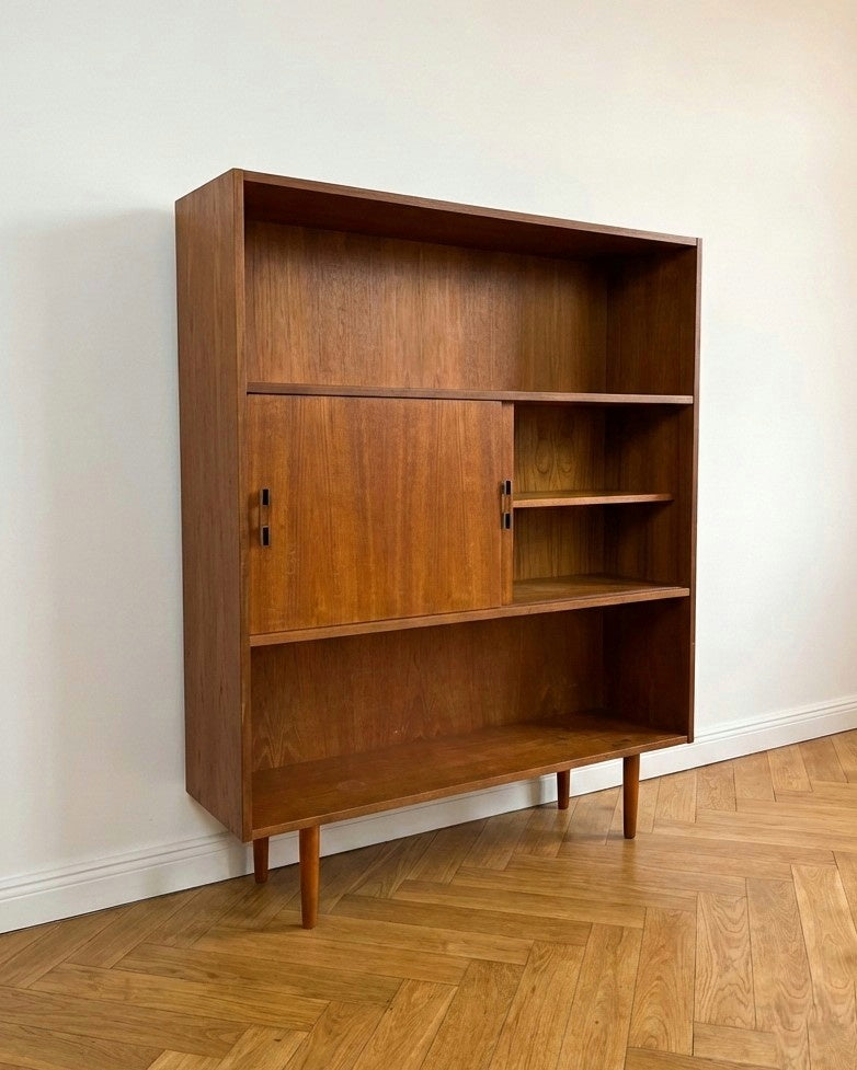 Libreria danese vintage anni 50 in teak, vista tre quarti, ripiani aperti superiore e inferiore con vano centrale a ante scorrevoli e maniglie 