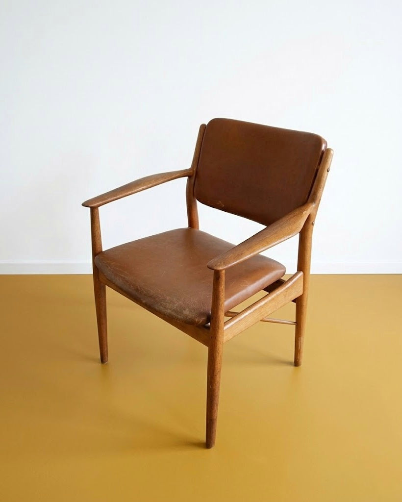 Poltroncina Arne Vodder danese anni 50 in teak, vista tre quarti, schienale avvolgente e braccioli integrati, rivestimento in pelle marrone
