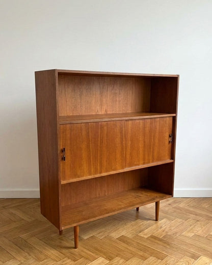 Libreria vintage danese anni 50 in teak, vista tre quarti destra, struttura a tre zone con ante scorrevoli centrali e gambe affusolate coniche